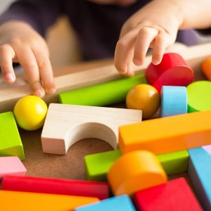 Delle mani di un bambino dell'asilo nido stanno per prendere delle colorate costruzioni in legno da una cassetta