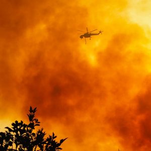 Elicottero in volo durante un incendio. Il cielo è interamente pieno di fumo e colorato d'arancione