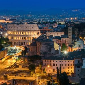 Roma, di sera, illuminata e vista dall'alto, con il Colosseo al centro dell'immagine