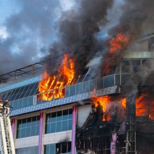 Un grande edificio commerciale o industriale con le fiamme che escono da alcune grandi finestre vetrate