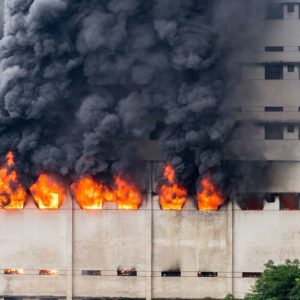 Un edificio in stile brutalista sta bruciando con fiamme che escono dalle finestre e fumo nero che si sprigiona verso l'alto