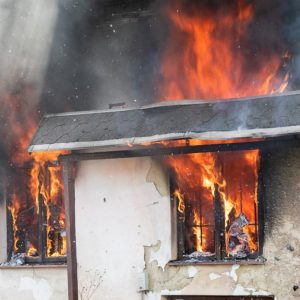 Dettaglio di una casa di campagna che brucia, con le fiamme che escono dalle due finestre