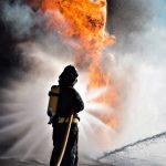 Un pompiere visto di spalle sta cercando di domare un incendio con un getto d'acqua