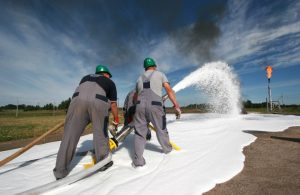 Tre uomini con caschetto protettivo verde stanno sparando schiuma su un incendio