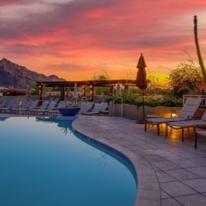 Piscina con sdraio in un villaggio turistico con vista panoramica sulle montagne, al tramonto