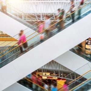 Vista laterale dell'incrocio tra due scale mobili, in un centro commerciale, con alcune persone sfocate per dare senso di movimento