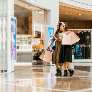 Due ragazze osservano una vetrina di un centro commerciale con delle buste di acquisti in mano